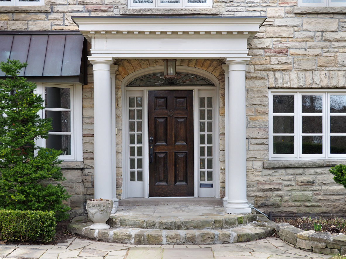 Elegant stone front entry with dark wood door, white sidelites and transom.