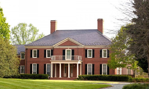 Example of a Georgian-Federal style house. This house has a traditional red brick facade, two chimneys, columns at the entrance, and grids on the windows.