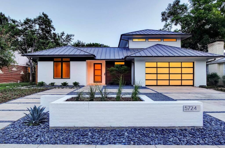 A modern home with a stucco facade, panel garage door, and a black standing seam metal roof.
