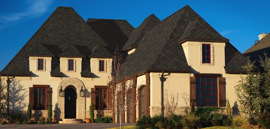 Light colored stuccoed home with wood trim and dark sienna shingles.