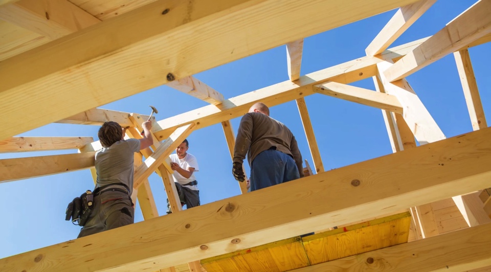 Three men work on the interior of a roof made with natural pine.